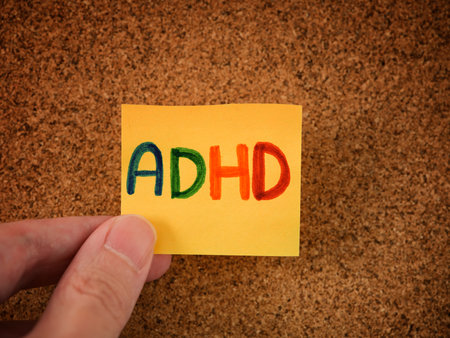 A man holding a yellow paper note with the abbreviation ADHD on it. ADHD is Attention deficit hyperactivity disorder. Close up.の写真素材