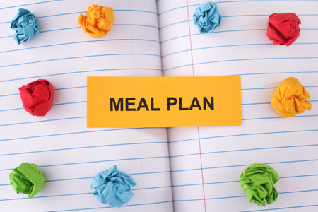 A paper note with the words Meal Plan on notebook sheet with some colorful crumpled paper balls around it. Close up.の写真素材
