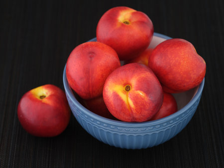 Freshly harvested nectarines in a blue bowl on a black mat. Low key. Close up.の写真素材