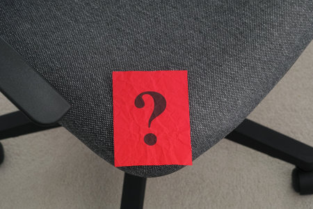 A crumpled red piece of paper with a question mark on it lying on an office chair. Close up.の写真素材