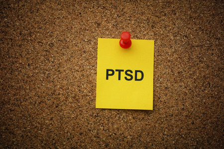 A yellow paper note with the abbreviation PTSD (Posttraumatic stress disorder) on it pinned to a cork board. Close up.の写真素材