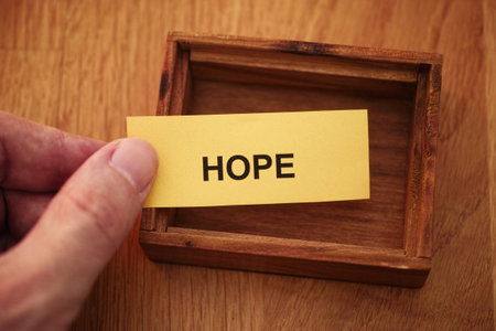 A man holding a piece of yellow paper with the word Hope on it in his hand over a small empty wooden box. Close up.の写真素材