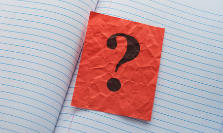 A crumpled red paper note with a question mark on it lying in an open notebook. Close up.