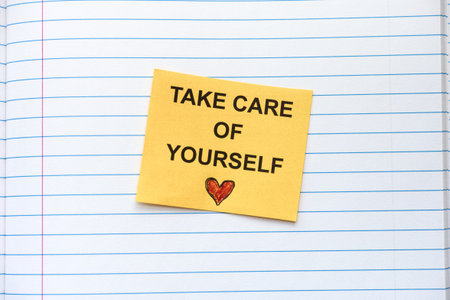 A yellow paper note with the words Take care of yourself on it lying in an open notebook. Close up.の写真素材