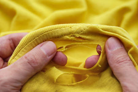 A man inspecting a ripped yellow t-shirt. Close up.の写真素材