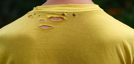 A close up shot of the back of a man wearing an old yellow t-shirt with holes in it. Close up.の写真素材