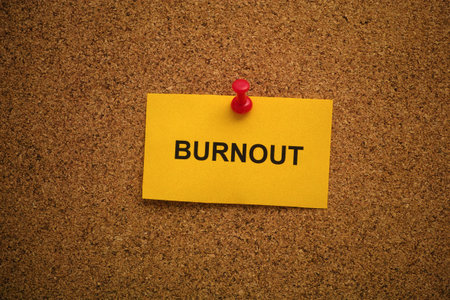 A yellow paper note with the word Burnout on it pinned to a cork board. Close up.の写真素材