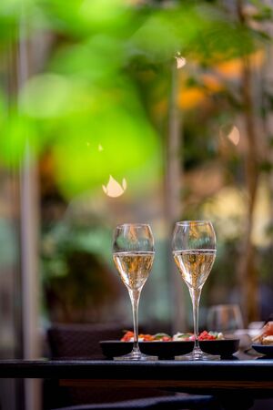 Two glasses of white wine with meal on summer terrace bokeh sunlight leaf cafeの写真素材
