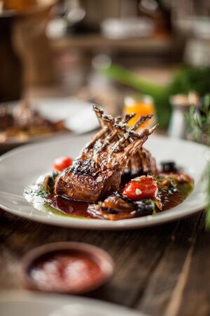 Plate with grilled ribs with sauce haute cuisine on wooden table in sunny daylight restaurantの写真素材
