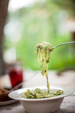 Fork with italian pasta on table on summer spring terrace on leaf bokeh side view daylight