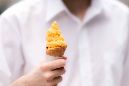 Young man wearing a white shirt is holding a delicious mango sorbet coneの写真素材