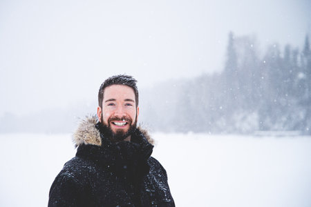 Portrait of a smiling young man in winter clothes on the background of a snowy forest