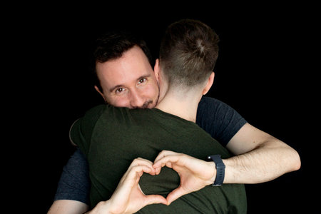 Young gay couple making a heart shape with his hands isolated on black background.の写真素材