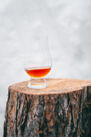 A glass of scotch whiskey on a wooden stump on a white snow backgroundの写真素材