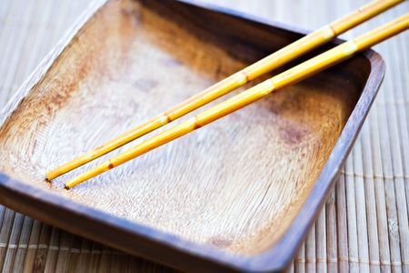 Empty wooden dish and wooden chopsticks on a bamboo mat. の写真素材