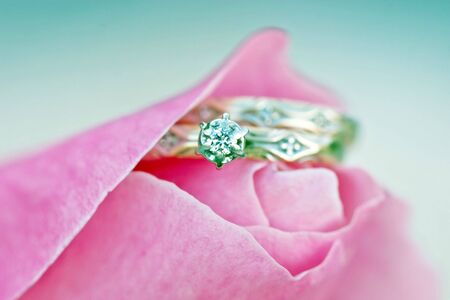 Engagement and wedding rings tucked inside of a soft pink rose. Focus on engagement stone. Soft focus on rose for effect.の写真素材
