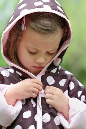 Little girl dresses herself in a raincoat.の写真素材