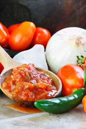 Rustic wooden spoon filled with spicy fresh salsa, surrounded by freshly picked and washed ingredients spilling from an old wooden bowl.の写真素材