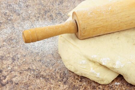 Close up of bread dough being rolled out on a stone counter top. の写真素材