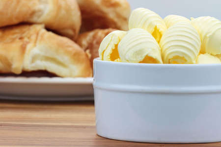 Curled butter in a dish with croissants in the background.の写真素材