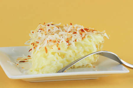 Slice of homemade coconut cream pie against a yellow background.の写真素材
