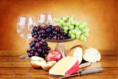 Dutch Edam cheese with fresh fruit, a loaf of whole grain bread and glasses of water.の写真素材