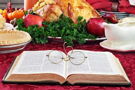 Open Bible with glasses lying on a holiday dinner table with prepared turkey and fixings in background.の写真素材
