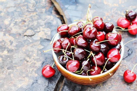 Bowl of black cherries with stems over a rustic background with available copy space.の写真素材
