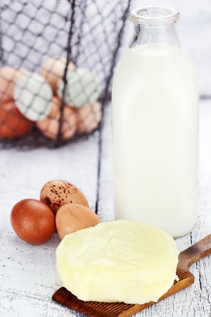 Farm fresh milk, butter, and eggs against a rustic background with basket of eggs. Milk is in a vintage glass milk bottle. Shallow depth of field.の素材 [FY31014234028]