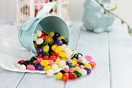 A blue tin bucket tipped over, spilling jelly beans onto a table  Shallow depth of field 