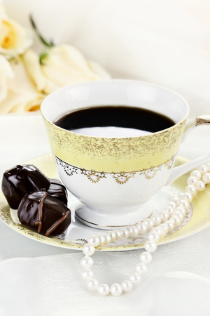 Close up of a cup of coffee chocolate candies and pearl necklace. Roses in the background. Shallow depth of field.の写真素材