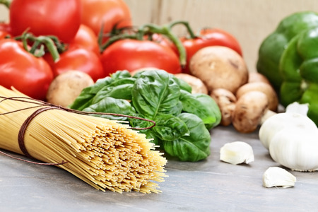 Italian cuisine ingredients of spaghetti, basil leaves, garlic, mushrooms, peppers and fresh tomatoes with extreme shallow depth of field.の写真素材