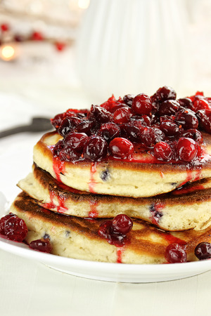 Cranberry sauce made with maple syrup, butter and fresh cranberries over delicious golden pancakes for Christmas morning. Extreme shallow depth of field with selective on pancakes.の写真素材