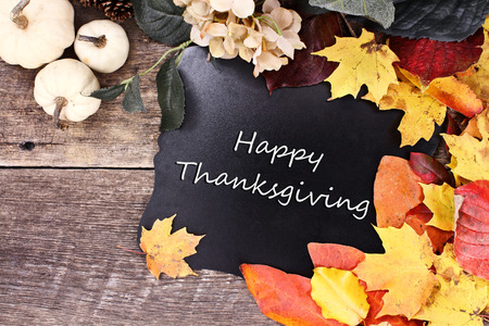 Chalk board with text Happy Thanksgiving surrounded by autumn leaves, flowers and white pumpkins over a rustic background.の写真素材