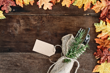 Silverware and burlap napkin with tag over rustic fall background of autumn leaves. Image shot from overhead.の写真素材