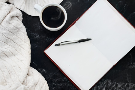 Soft knit sweater blanket with a hot cup of coffee and an open book with pen over grungy chalkboard ...