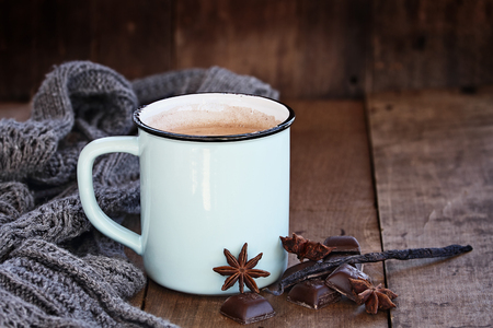 Enamel cup of hot cocoa or coffee for Christmas with chocolate bars, vanilla pod, spices and gray scarf against a rustic background. Shallow depth of field with selective focus on drink.の写真素材