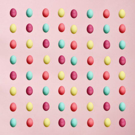 Rows of colorful Easter eggs isolated over a pink background. Flat lay style.