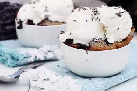 Two bowls of freshly baked homemade blueberry lavender cobbler topped with vanilla ice cream. Selective focus on dish in foreground with extreme shallow depth of field. Perfect dessert for spring or summer.の写真素材