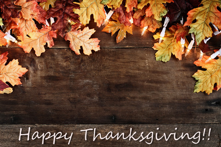 Rustic fall background of autumn leaves and decorative lights with Happy Thanksgiving text over a rustic background of barn wood. Image shot from overhead.の写真素材