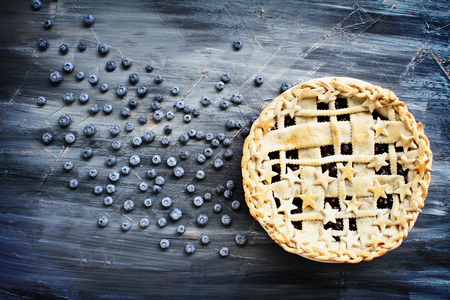 Top view of a blueberry pie with lattice and stars crust and fresh berries scattered across artistic wooden background.の写真素材