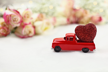 1950's antique vintage red truck hauling a glittery red heart past a roll of beautiful long stem roses. Extreme shallow depth of field with selective focus on vehicle.の写真素材