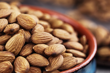 Close up of raw whole almonds in bowl and wooden spoon against a rustic background.の写真素材
