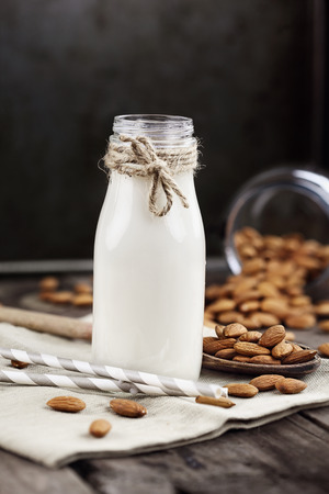 Organic white almond milk in a glass bottle with whole almonds spilled over a rustic wooden table.の写真素材
