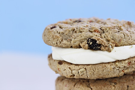 Macro of Carrot cake raisin cookie sandwiches stuffed with cream cheese icing agaist a blue...