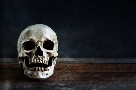 Halloween human skull on an old wooden table in front of black background with free space for text.の写真素材
