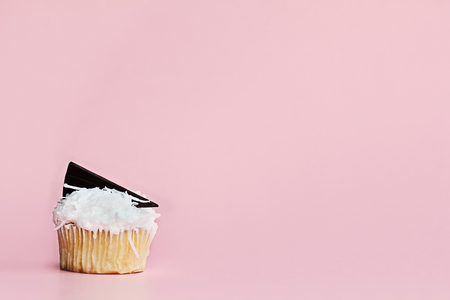 Pretty coconut frosted cupcake decorated with a wedge of chocolate against a pink background.の写真素材