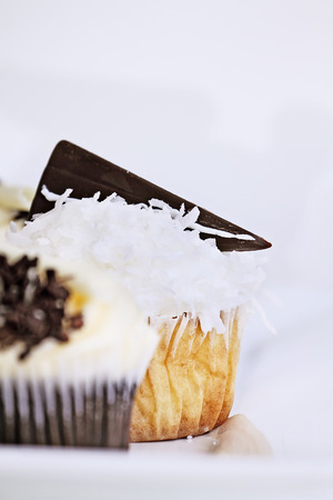 Pretty coconut frosted cupcake decorated with a wedge of dark chocolate. Extreme shallow depth of field with selective focus on center cupcake.の写真素材
