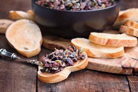 Homemade mixed Olive Tapenade made with garlic, capers, olive oil, Kalamata, black and green olives spread over toasted bread. Extreme shallow depth of field with selective focus on center canape.の写真素材