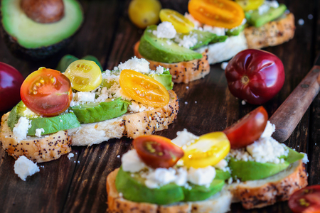 Avocado toast sandwich with avocados, fresh from the garden heirloom tomatoes and feta cheese, Greek food and healthy vegetarian diet concept, over a rustic wooden background.の写真素材